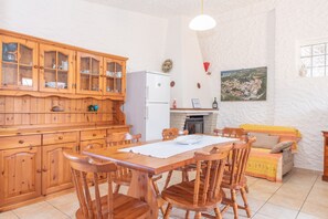 Un comedor con una mesa y sillas de madera, un mueble de madera con puertas de cristal, un refrigerador, un sofá y una chimenea.