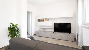 A modern living room with a grey sofa, a flat-screen TV on a grey cabinet, a potted plant, and a bookshelf. - Modern apartment near Lake Garda with Wi-Fi and terrace (BARDOLINO)