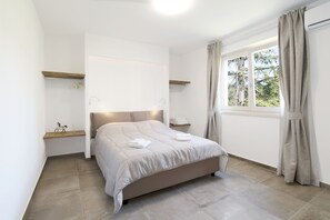 A bedroom with a bed, a window with curtains, a bedside table, and a shelf.