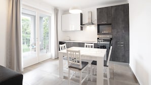 A modern kitchen with white cabinetry, a dining table with chairs, and a large window with a view of greenery. - Modern apartment near Lake Garda with Wi-Fi and terrace (BARDOLINO)