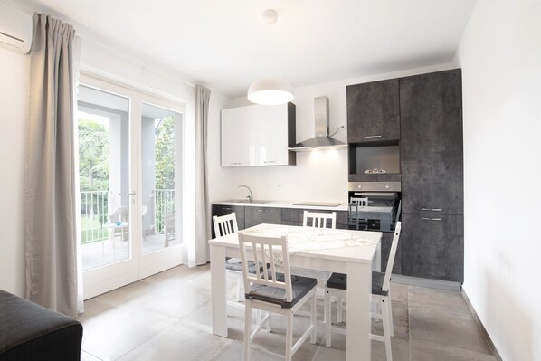 A modern kitchen with white cabinetry, a dining table with chairs, and a large window with a view of greenery.