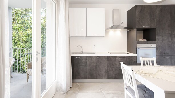 A modern kitchen with a balcony, white cabinets, and a dining area. - Modern apartment near Lake Garda with Wi-Fi and terrace (BARDOLINO)