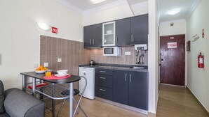 A compact kitchen with a microwave, a small refrigerator, and a dining area with a table and chairs. - Sunny Albufeira Beach Studio with Wi-Fi, Balcony, and Close to the Beach (Albufeira)