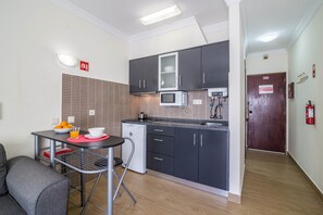 A compact kitchen with a microwave, a small refrigerator, and a dining area with a table and chairs. - Sunny Albufeira Beach Studio with Wi-Fi, Balcony, and Close to the Beach (Albufeira)