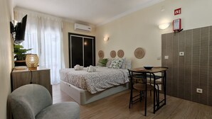 A bedroom with a bed, bedside table, chair, and a small dining table with chairs. - Sunny Albufeira Beach Studio with Wi-Fi, Balcony, and Close to the Beach (Albufeira)