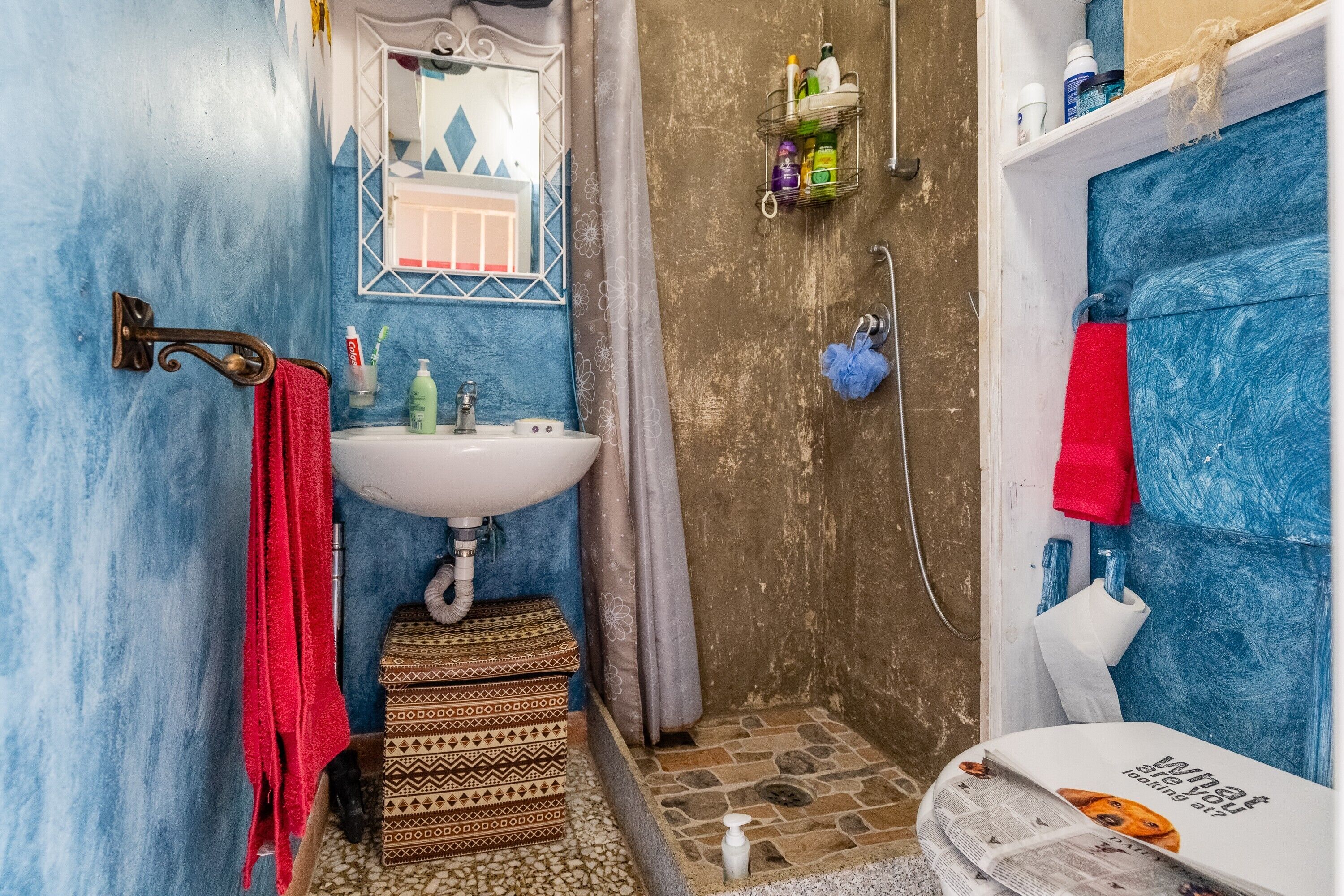 A bathroom with a white sink, a mirror, a shower area, and a red towel.