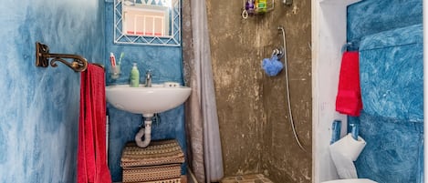 A bathroom with a white sink, a mirror, a shower area, and a red towel.
