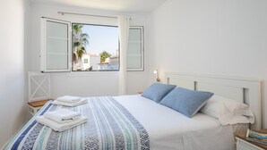 Un dormitorio con cama, una ventana con cortinas, una mesita de noche y un velador.