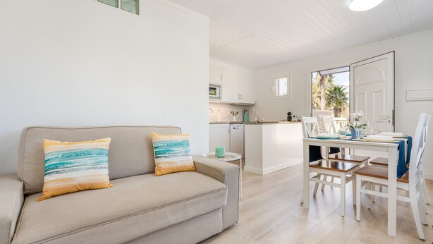 Una sala de estar moderna con sofá, una mesa de comedor con sillas, una zona de cocina y vistas a través de un ventanal.