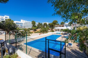 Una piscina con área vallada, rodeada de vegetación y edificios.