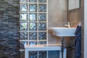 Un baño con lavamanos blanco, cabina de ducha de vidrio y pared de piedra.