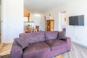 Ein Wohnzimmer mit einem violetten Sofa, einem an der Wand befestigten Fernseher und einem Holzschrank.
