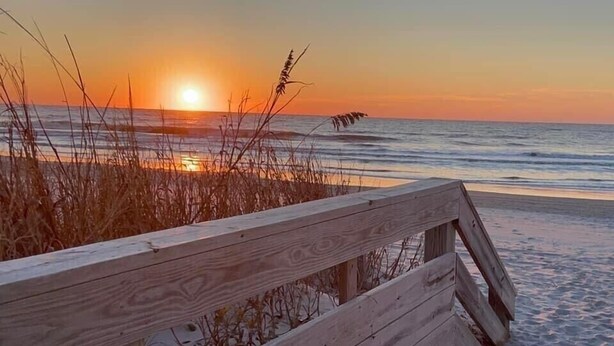 Un muelle de madera que conduce a una playa con un atardecer de fondo.