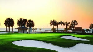 Un campo de golf con búnkeres de arena, palmeras y un edificio al fondo.