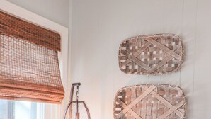 Un sillón color turquesa con un cojín tejido, una mesita con una planta en maceta, y dos adornos de pared tejidos.