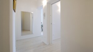 Un couloir avec une porte blanche, un miroir et un interrupteur sur le mur.