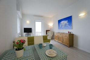 A living room with a sofa, a dining table with a vase of flowers, a television, and a wooden cabinet.