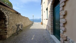 Une ruelle étroite pavée de pierres, avec un vélo garé sur le côté gauche, un mur de pierre d’un côté et un bâtiment avec une porte verte de l’autre.