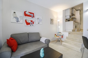 A modern living room with a grey sofa, a coffee table, and a staircase leading to a kitchen area.