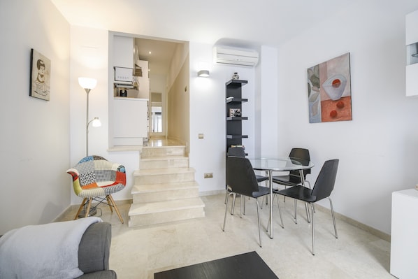 A modern living space with a staircase, a dining area with chairs, a colorful chair, a sofa, and a wall-mounted artwork.