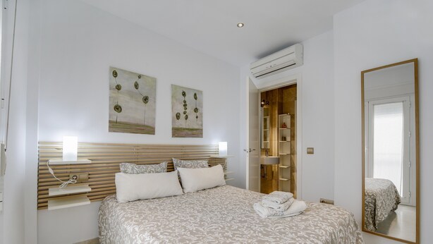 A bedroom with a large bed, a bedside table, a mirror, and artwork on the wall. - Modern Apartment "Torre Close" to Beach in Historic Centre with Balcony and Air Conditioning (Cádiz)