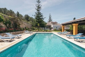 A rectangular swimming pool with clear blue water, surrounded by lounge chairs and a stone wall with vegetation. - Beautiful Estate with Mountain View, Pool, Wi-Fi and Air Conditioning (Santa Eulalia del Río)