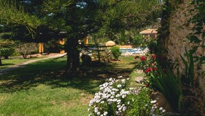 Ein Garten mit einem Pfad, Bäumen und einem Gebäude im Hintergrund, das einen Pool beinhaltet.