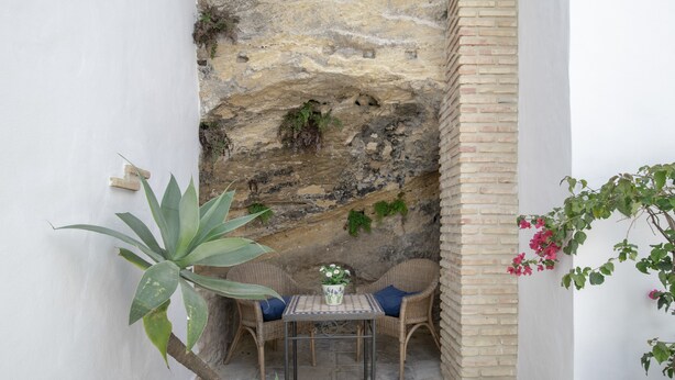 Une petite terrasse avec une table et deux chaises en osier, une plante en pot et un mur de pierre.