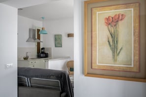 Ein Zimmer mit einem Bett, einem gerahmten Gemälde, einer Küchenzeile und einer Pendelleuchte.