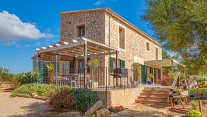 A stone building with a covered porch, steps leading to the entrance, and a garden with various plants. - Stunning Villa Can Xesquet with Mountain View, Wi-Fi (ses salines)