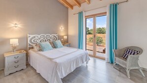 A bedroom with a bed, nightstands, a chair, and a view through a glass door. - Stunning Villa Can Xesquet with Mountain View, Wi-Fi (ses salines)