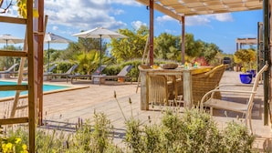 A wooden deck with a pool, lounge chairs, and a covered seating area with a table and chairs. - Stunning Villa Can Xesquet with Mountain View, Wi-Fi (ses salines)