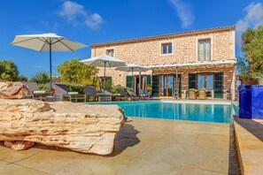 Ein Steinhaus mit Pool, Sonnenschirmen und Liegestühlen.