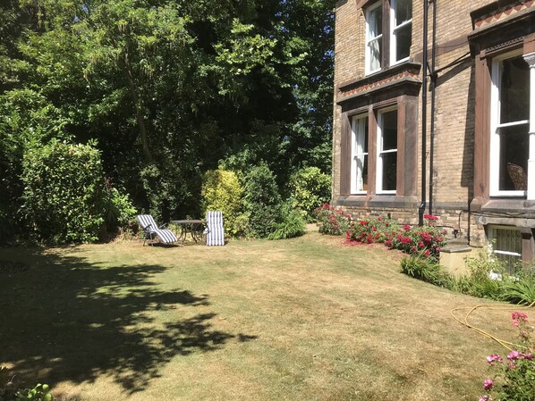 A well-maintained garden with a lawn, two striped lounge chairs, and a brick building with large windows.