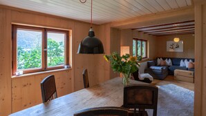 Een houten hut binnen met een eettafel, stoelen, een bank en een hanglamp.