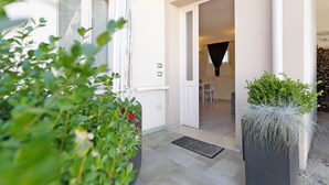 A building entrance with a door, a potted plant, and a visible interior space with a chair and a table. - The Magnolia Three-Room Apartment: Charm on Three Levels in Lonato del Garda’s Courtyard (Lonato del Garda)