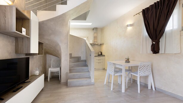A modern living space with a flat-screen TV, white furniture, a staircase, and a kitchen area. - The Magnolia Three-Room Apartment: Charm on Three Levels in Lonato del Garda’s Courtyard (Lonato del Garda)
