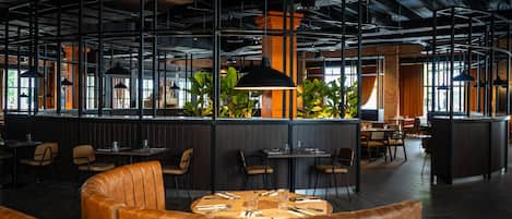 A modern restaurant with high ceilings, exposed ductwork, and a mix of seating arrangements including booths and tables.