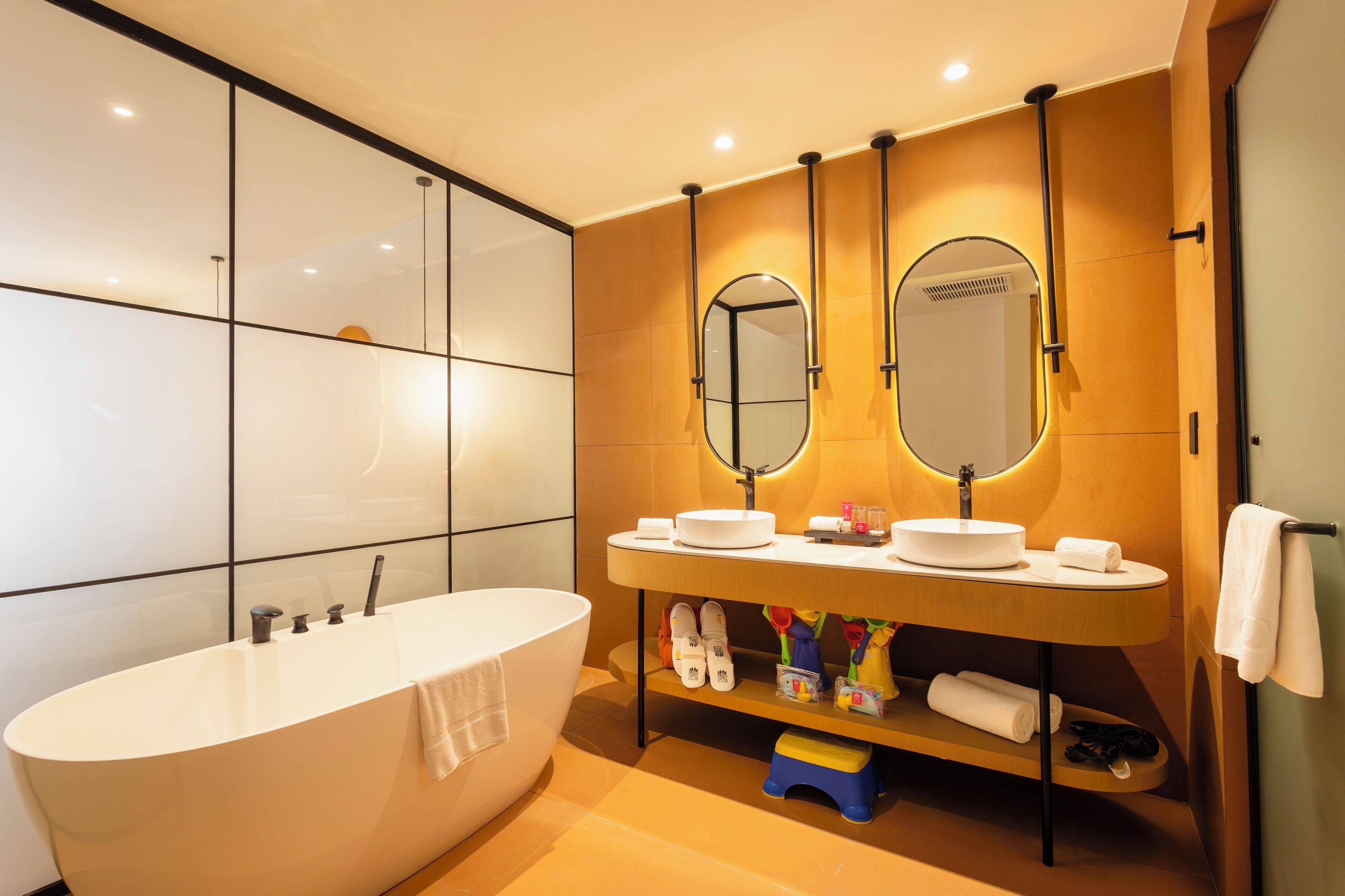 A modern bathroom with a freestanding bathtub, a vanity with two mirrors, and a shelf with toiletries.