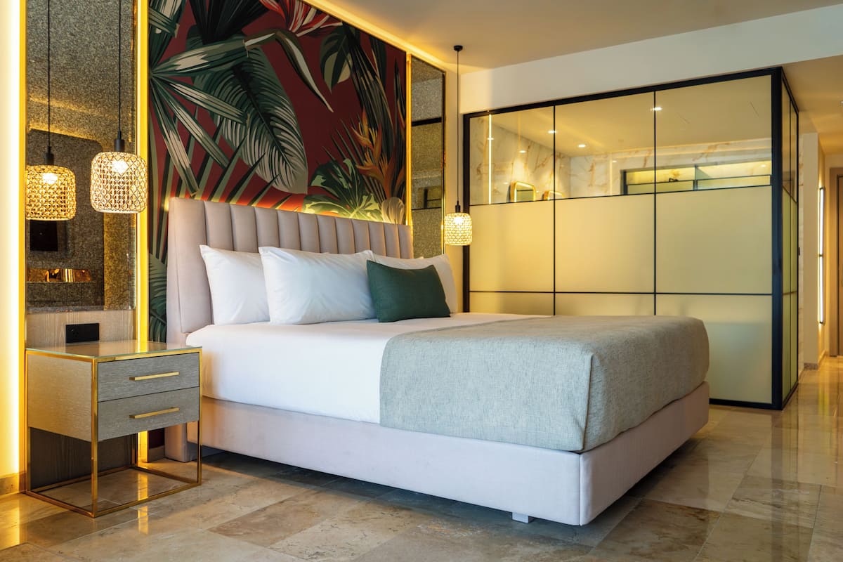Een moderne slaapkamer met een groot bed, nachtkastjes, een spiegel en een muur met een tropisch thema.
