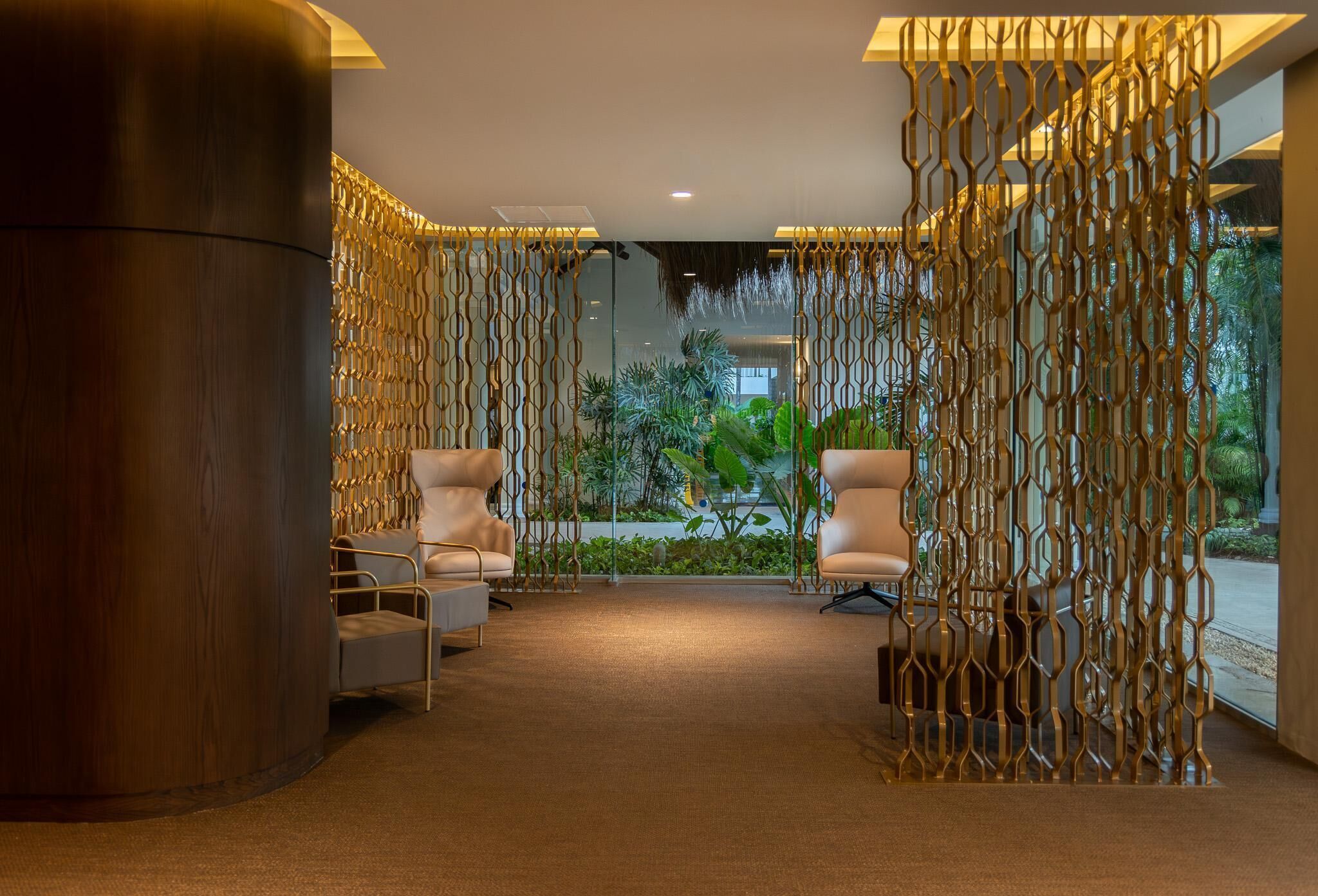 Eine moderne Lobby mit einer geschwungenen Holzsäule, zwei weißen Sesseln, einer strukturierten Wand und Blick auf Grünflächen.