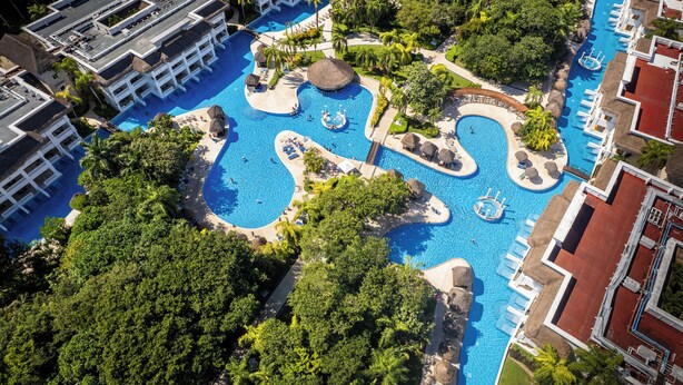 Vista aérea de un resort con múltiples piscinas, exuberante vegetación y edificios del complejo.