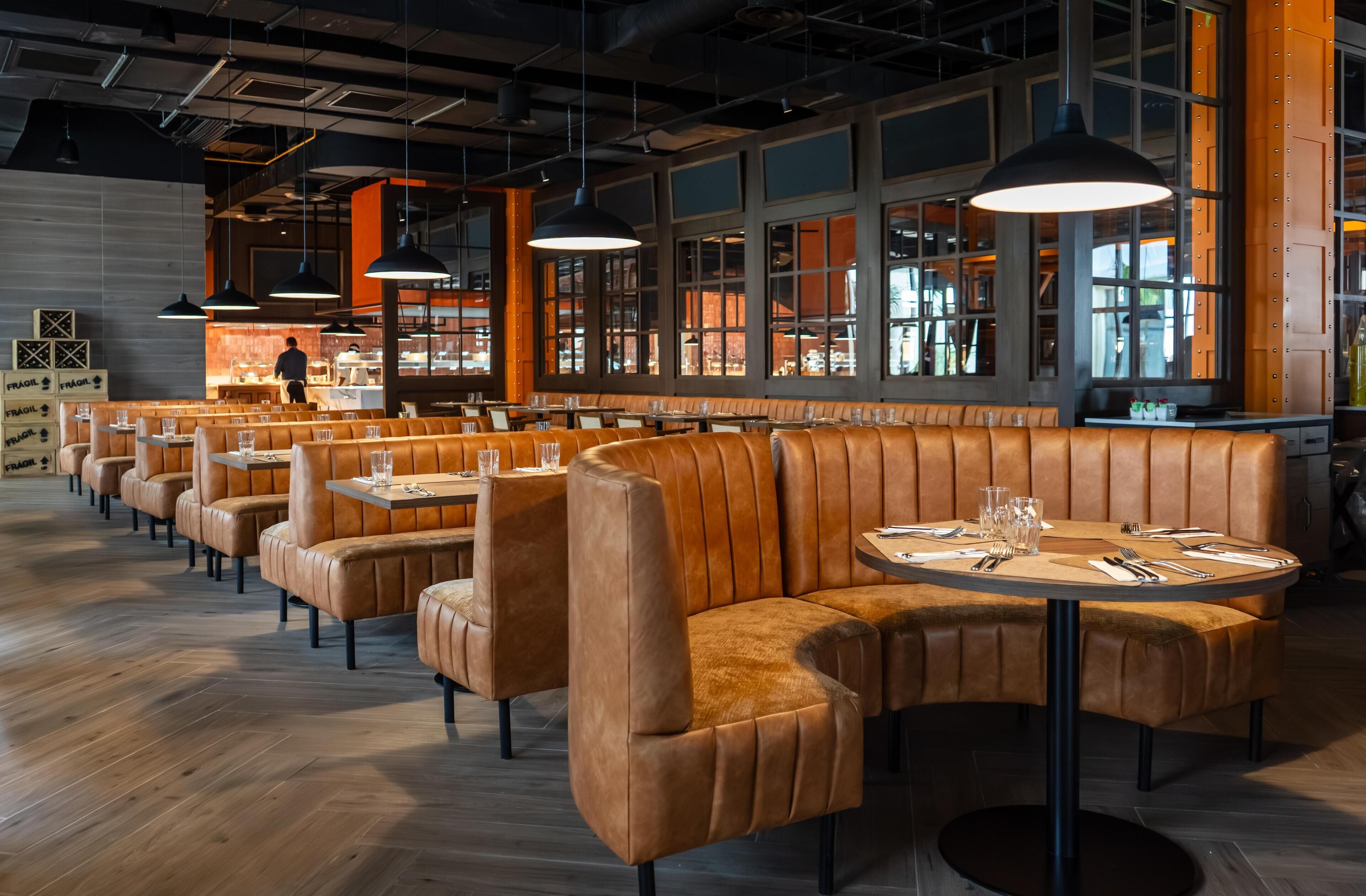 Un interno ristorante moderno con sedute in pelle, tavoli rotondi, luci a sospensione e ampie finestre.