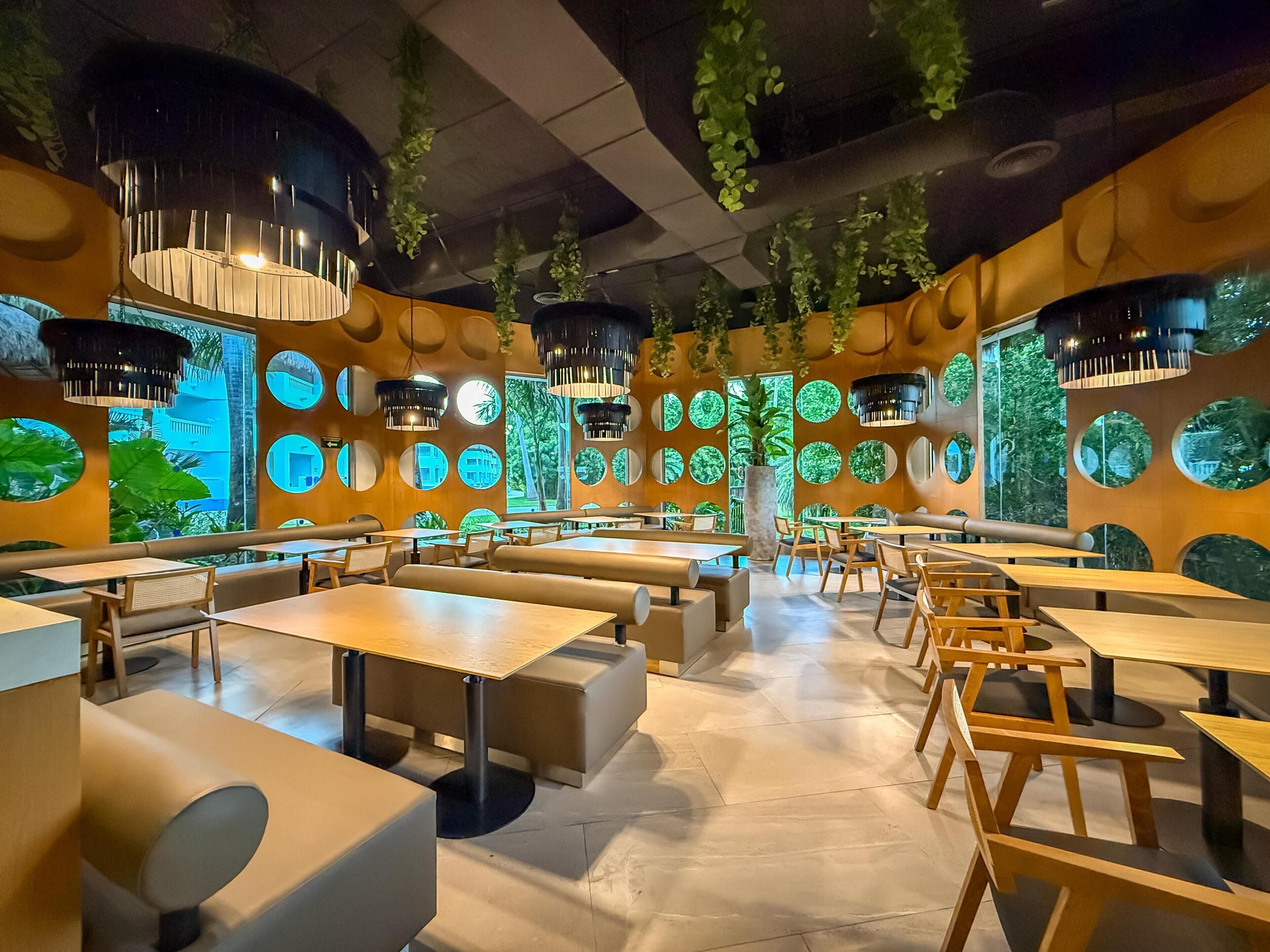 A modern restaurant interior with round tables, booths, and hanging plants.
