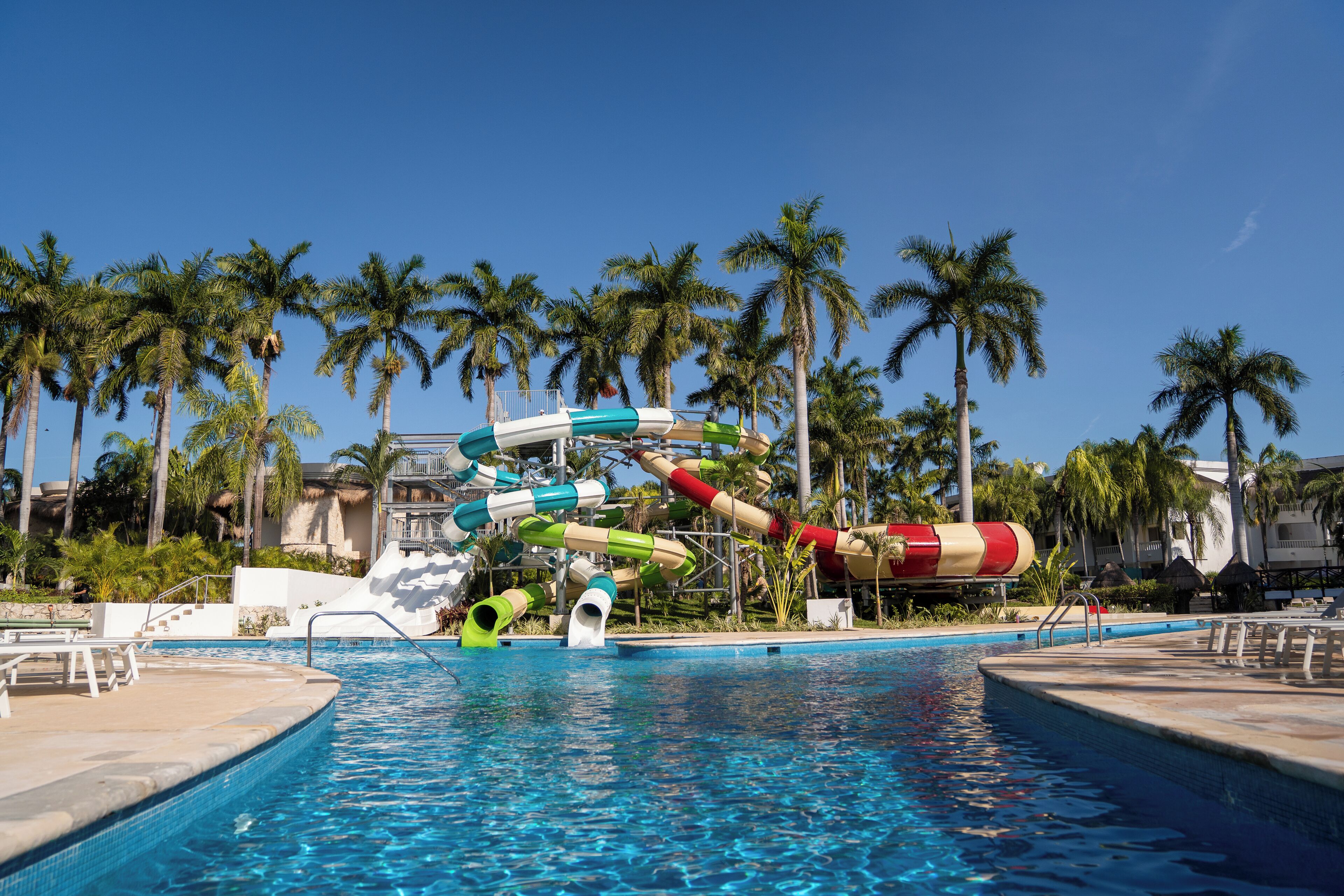 A swimming pool with water slides and palm trees in the background.
