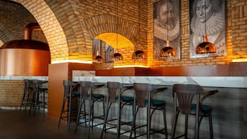 A brick-walled bar area with a large oven, bar stools, and framed portraits on the wall.
