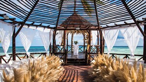 Un pabellón frente a la playa con un escenario, cortinas blancas y plumas de pampa.