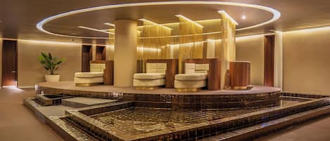 A modern lobby with a central seating area, a water feature, and a reception desk.
