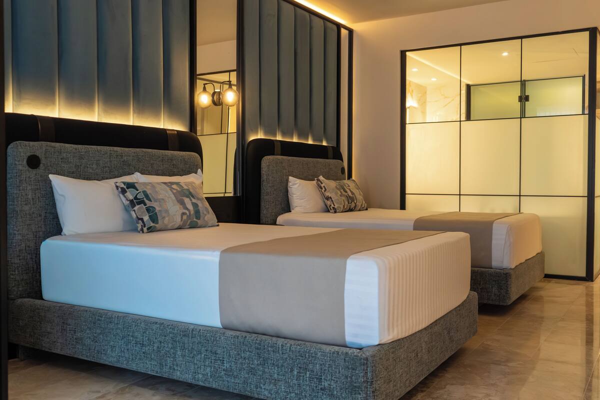 Een moderne hotelkamer met twee bedden, een grote spiegel en een schuifglazen deur.