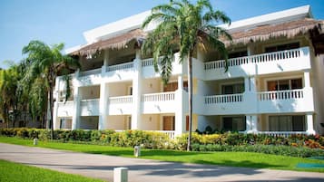A multi-story hotel with a white facade, thatched roof balconies, and lush landscaping.